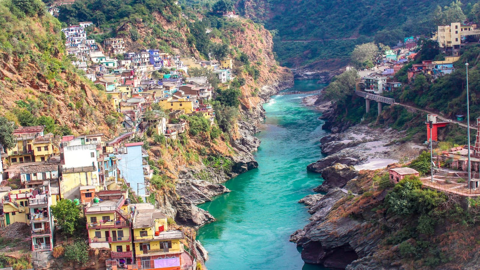 Scenic view of a river flowing through Uttarakhand town with hills and colorful houses