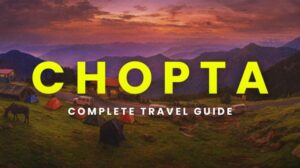 Tents and small cottages on a green hillside in Chopta with a mountainous backdrop at sunset, showcasing a serene camping scene.