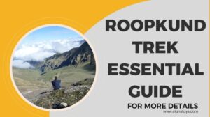 A trekker sitting on a rocky slope overlooking vast green valleys and clouds during the Roopkund Trek in the Himalayas.